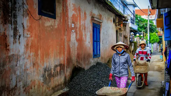 Deux femmes poussent des brouettes dans une ruelle de Hoi An, au Vietnam