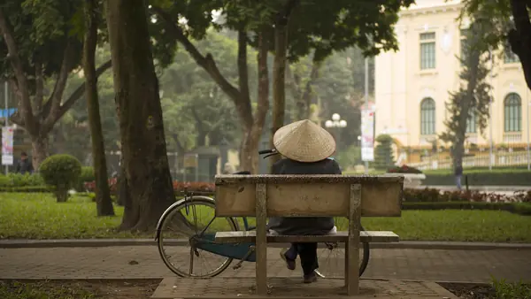 Une personne coiffée d'un chapeau conique assise sur un banc, dans le quartier de Ba Dinh, à Hanoi